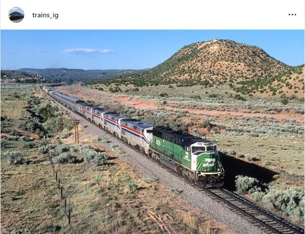 Instagram post from "trains_ig" picture of Amtrack train being pulled by a green engine.