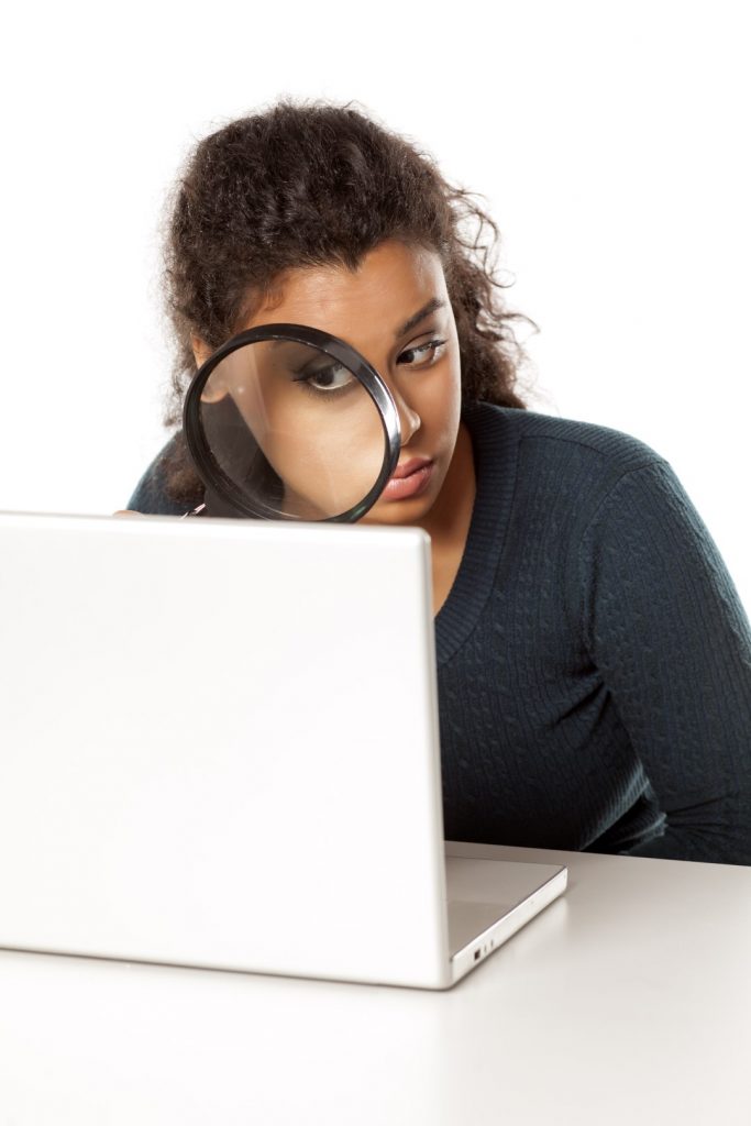 portrait of young woman with magnifying glass looking in her laptop on a white background