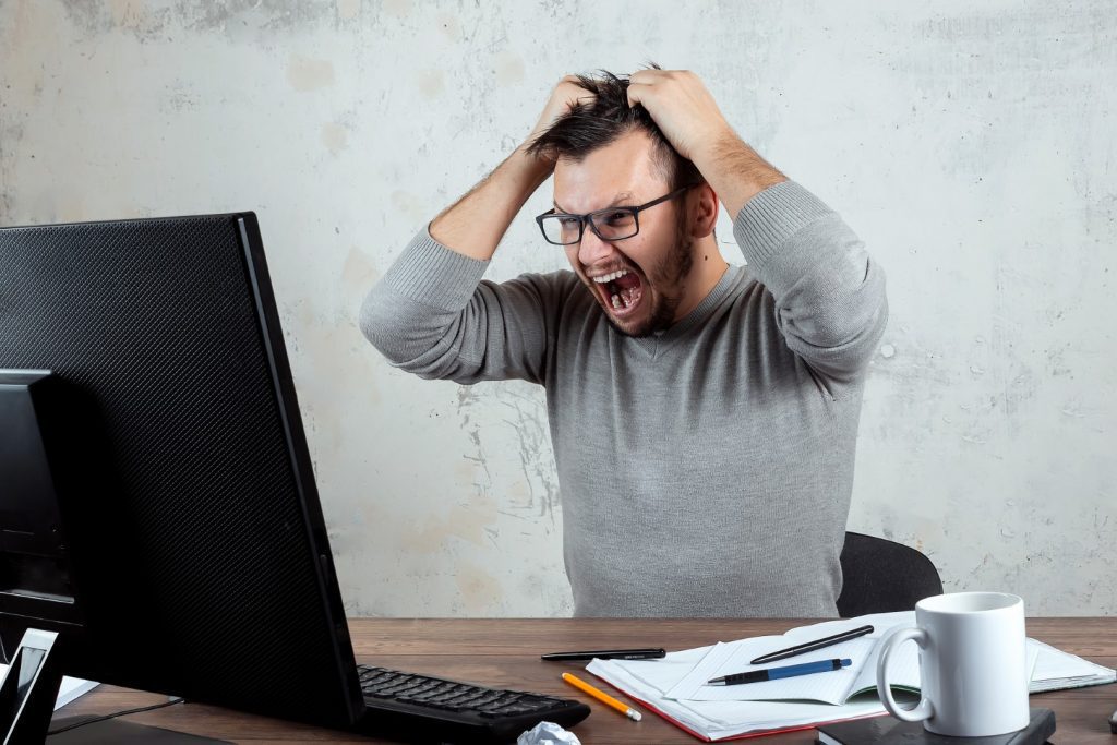 frustrated and saddened man at computer pulling his hair out.