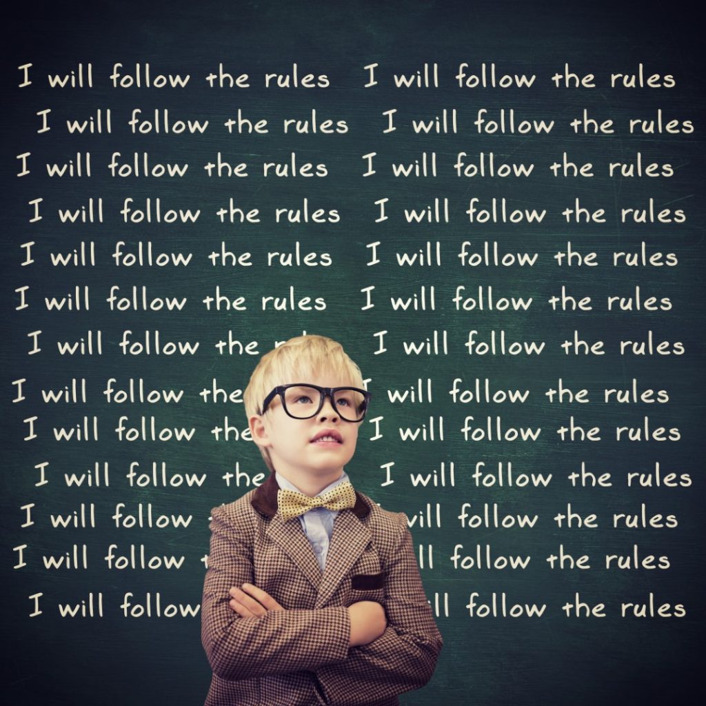 Oby standing in front of a chalk board with the sentence "I will follow the rules" written multiple time.